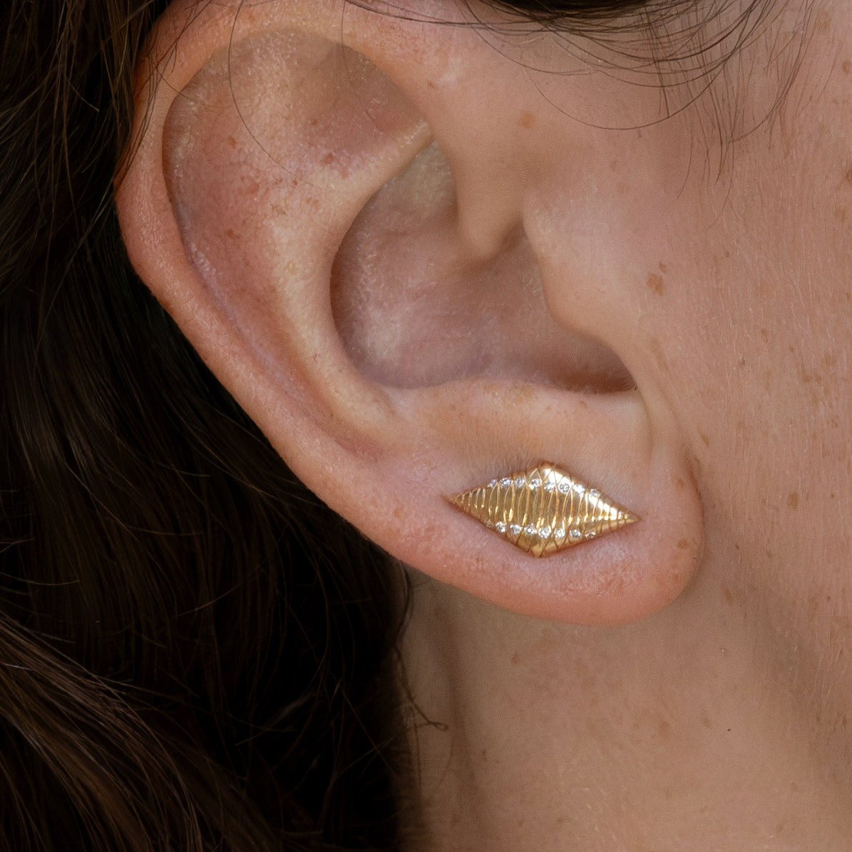 Close-up of a geometric 14k gold earring, resembling a pointed diamond with delicate engravings and sparkling 0.8mm round lab-grown white diamonds. A bold yet refined design perfect for elevating everyday style.