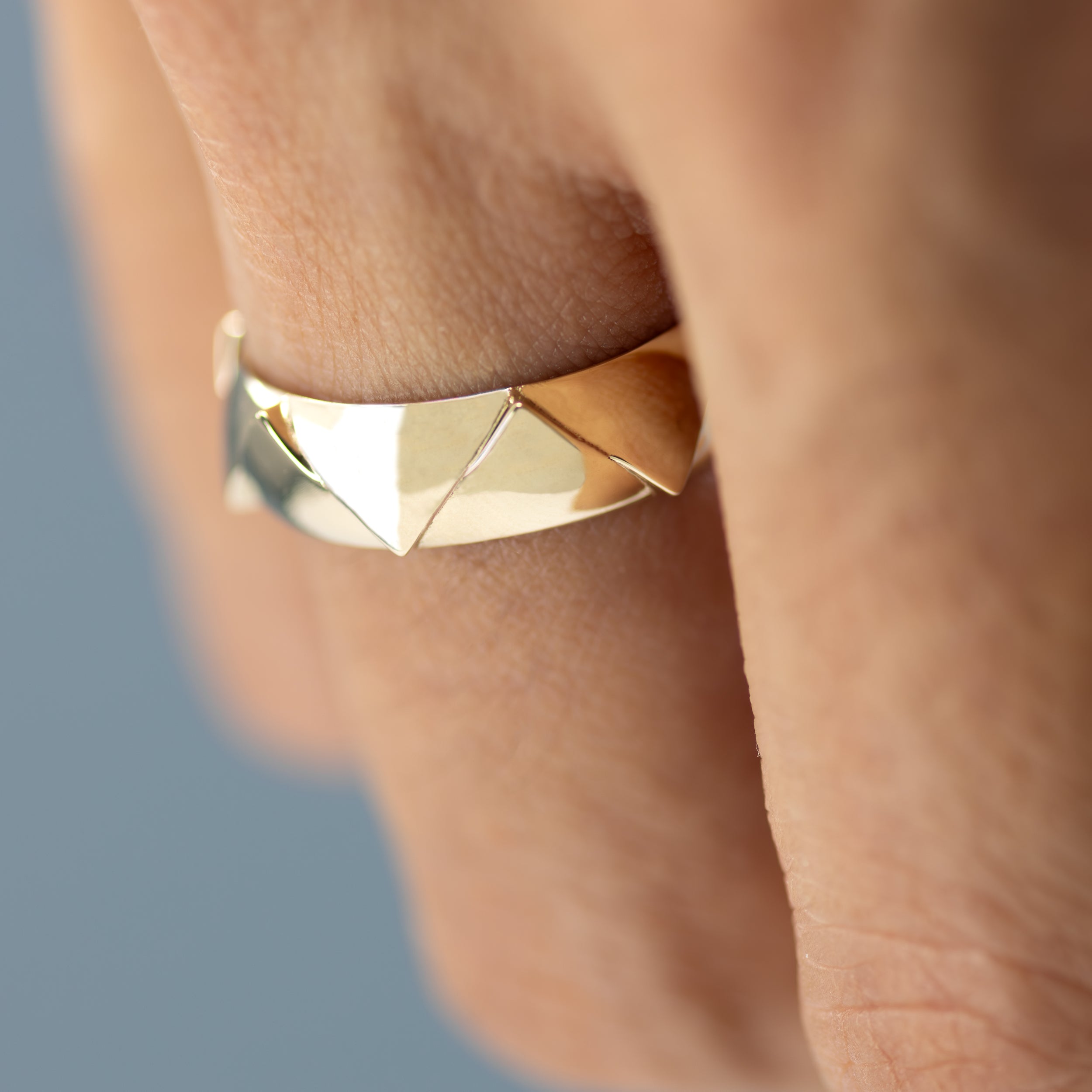 Close-up of a solid 14k gold ring featuring crown-like facets, reflecting light with brilliance and showcasing its bold and refined design. Band width: 5.7mm