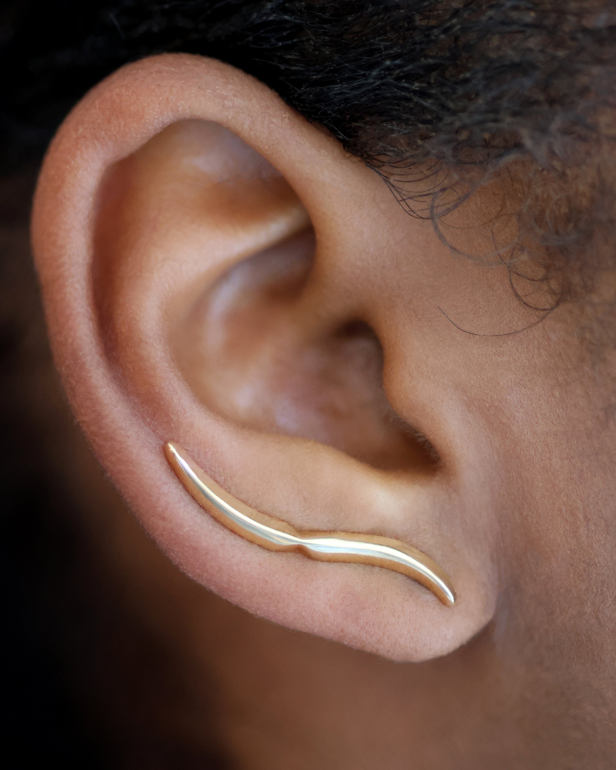 The Lance Crawler, a single solid 14k gold earring featuring a sleek, curved design. The minimalist piece elegantly follows the natural contour of the ear, showcasing its polished finish and bold, modern aesthetic.