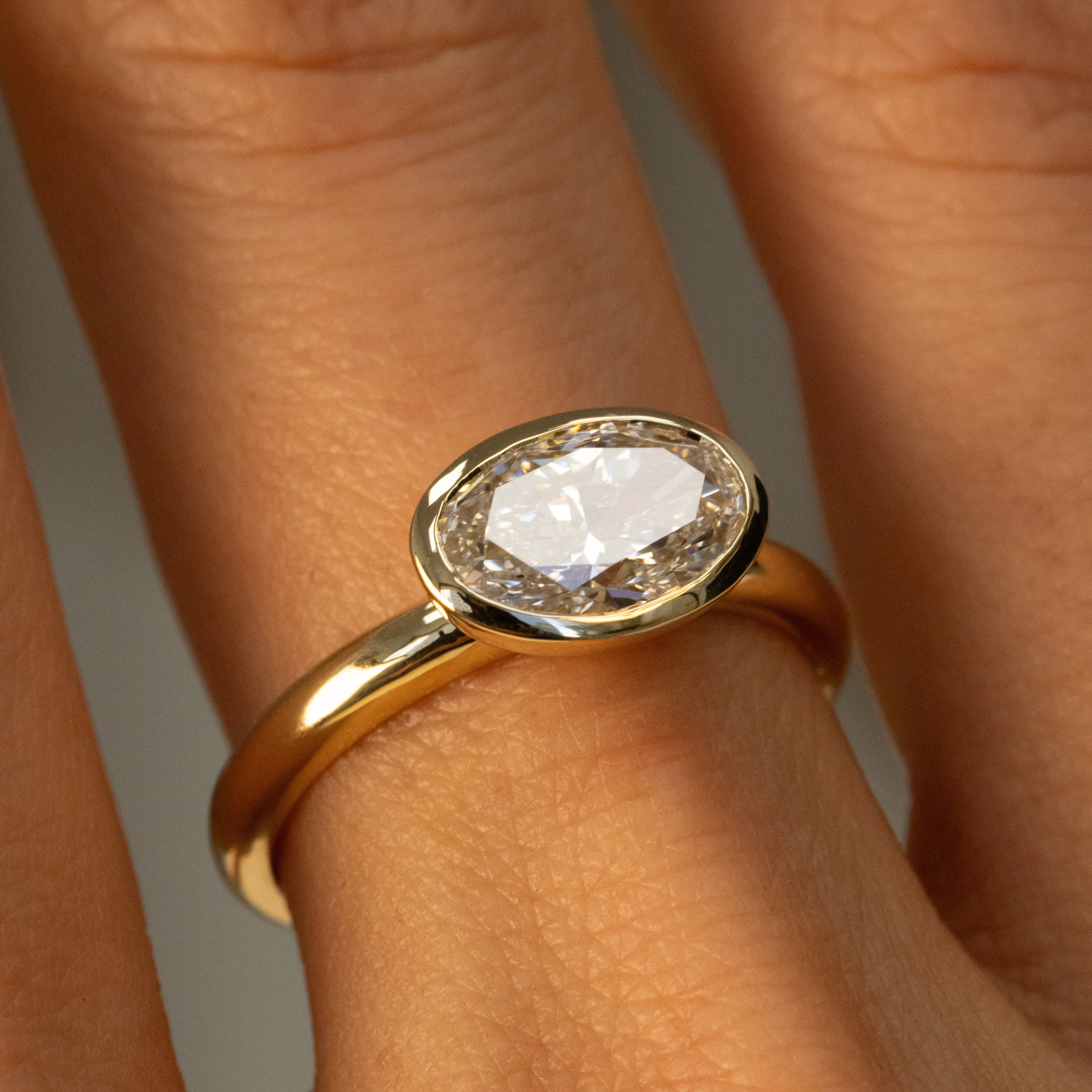 A close-up of a gold ring with a oval-shaped clear gemstone, worn on a person's finger.