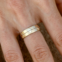 A close-up of a hand wearing two solid 14k gold geometric rings stacked together. The rings feature recessed triangular patterns and a polished finish, offering a cohesive and modern design. 