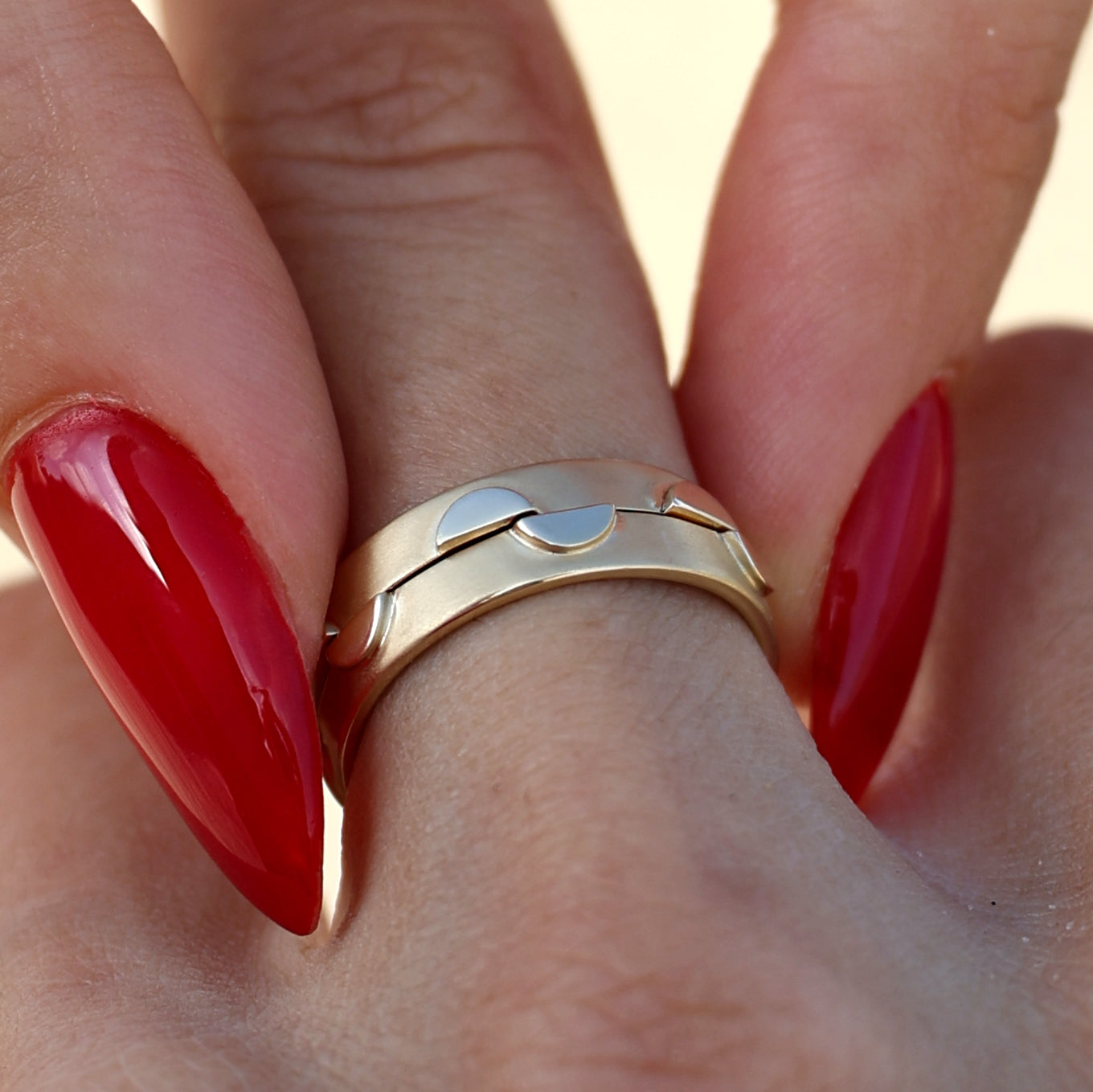 Close-up of two solid 14k gold rings stacked together on a hand with red polished nails. The rings feature circular cutout designs and a polished finish, offering a playful and modern aesthetic as part of a dynamic pair.