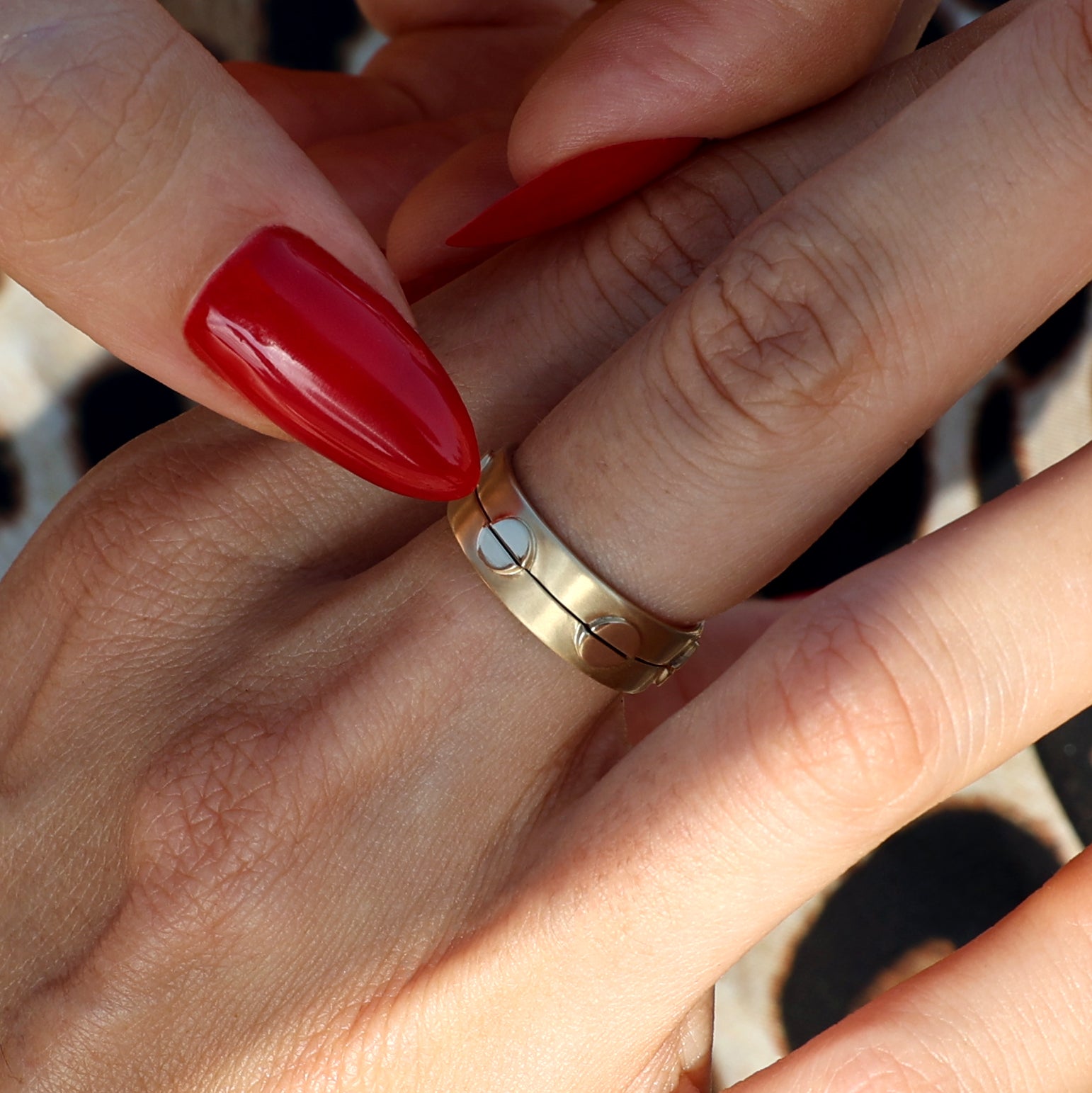 Close-up of two solid 14k gold rings stacked on a finger, featuring circular cutout designs and a polished finish. The rings are shown being adjusted with hands adorned with red nails.