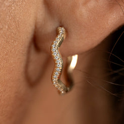 Gold wavy huggie earring with small diamonds worn by a person