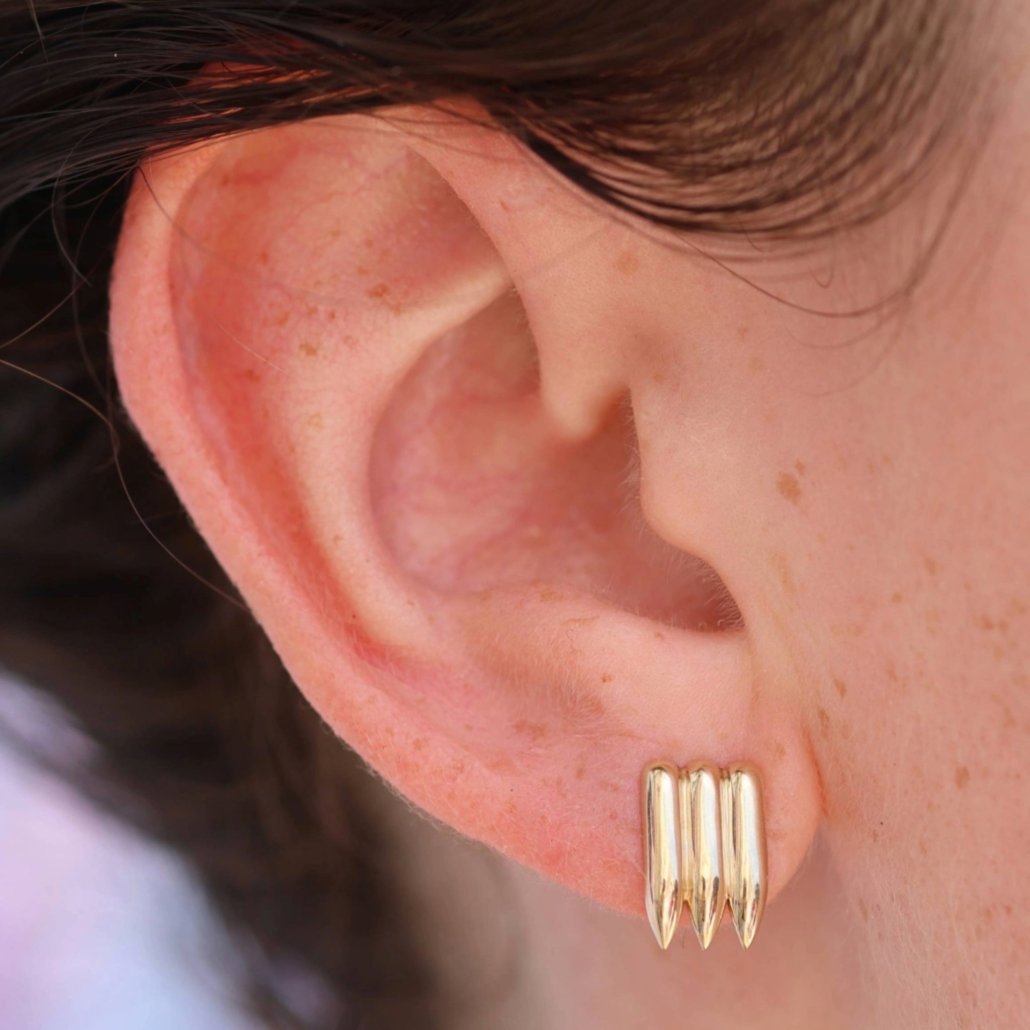 A pair of solid 14k gold stud earrings featuring a unique triple-bullet design with pointed ends. The earrings have a polished finish that enhances their modern and bold aesthetic.