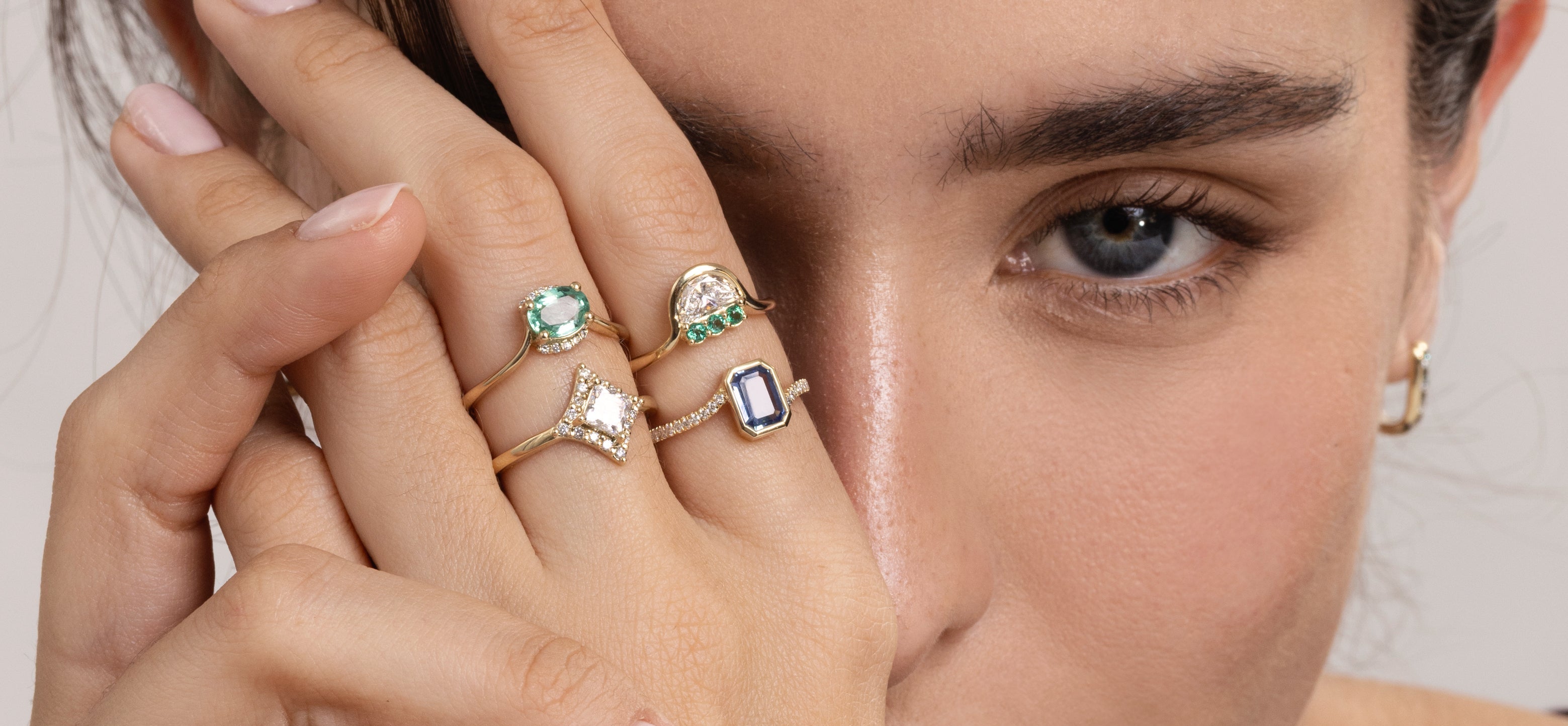 Close-up of a woman's face with three rings on her fingers, featuring different gemstones.