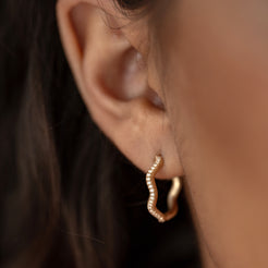 Close-up of a 14k solid gold hoop earring featuring a fluid, wave-like design, elegantly encrusted with sparkling 0.8mm lab-grown white diamonds. A bold yet graceful addition to any look. 