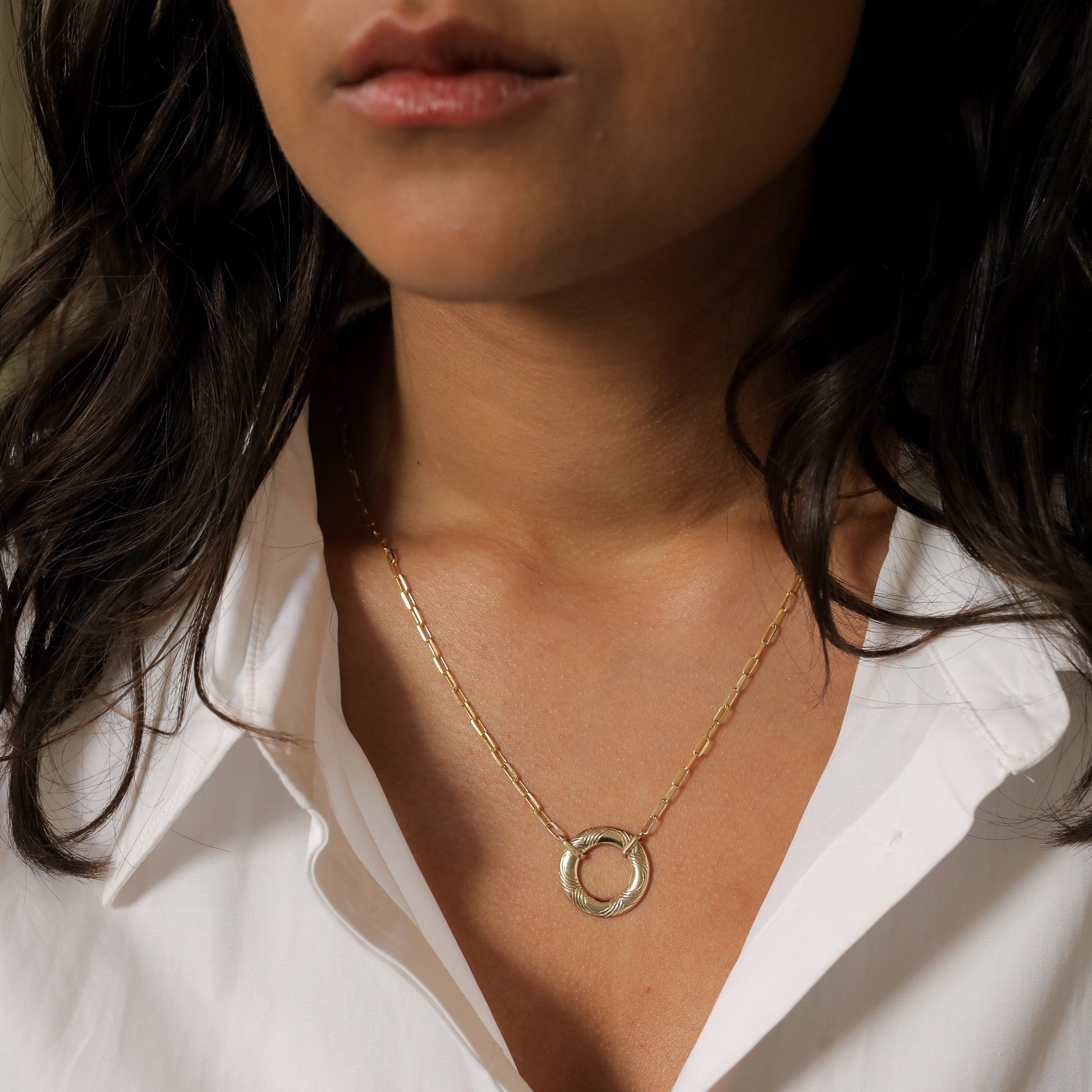 The Lifebuoy Necklace, a solid 14k gold pendant with intricate engraved details, paired with a gold paperclip link chain. The sleek and modern design adds an elegant touch to her look.